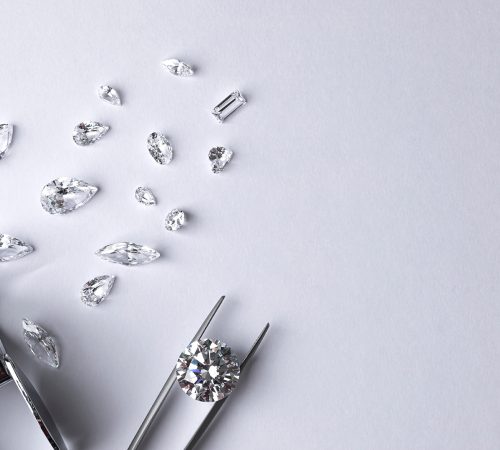 Top view of Diamonds of different cuts and sizes scattered on table with a magnifying glass and tweezers on white background.